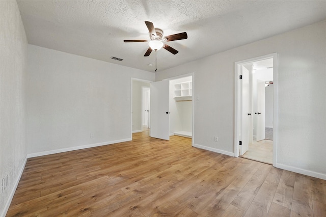 unfurnished bedroom featuring a spacious closet, ensuite bath, light wood finished floors, baseboards, and visible vents