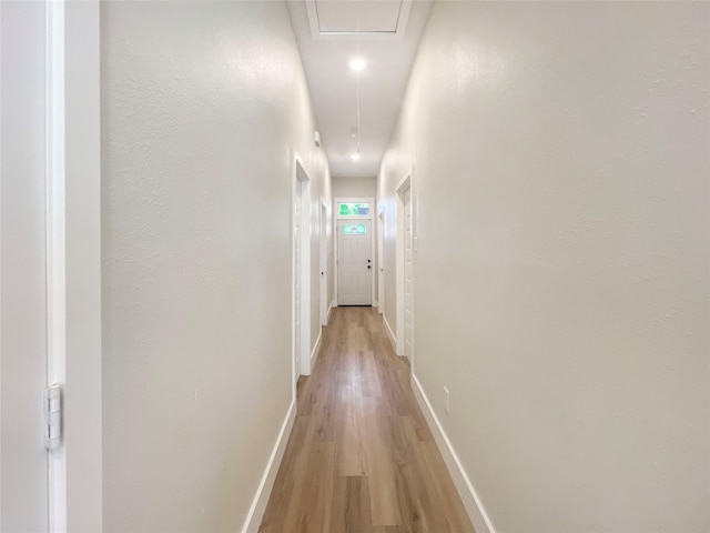hallway featuring light wood-type flooring, attic access, and baseboards