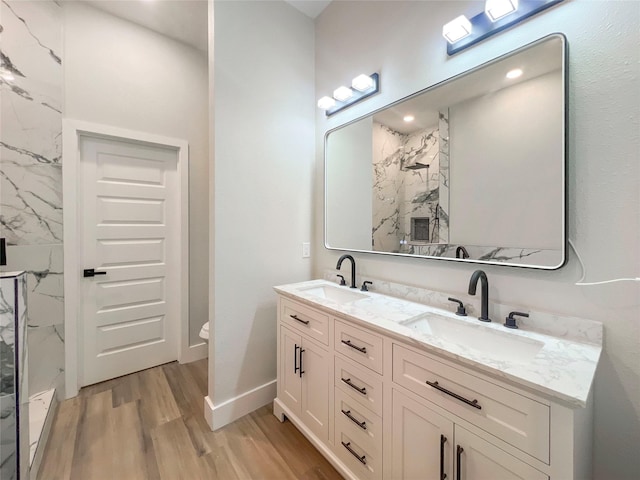 full bath featuring double vanity, wood finished floors, a marble finish shower, and a sink