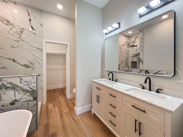 full bathroom with double vanity, wood finished floors, a soaking tub, and a sink