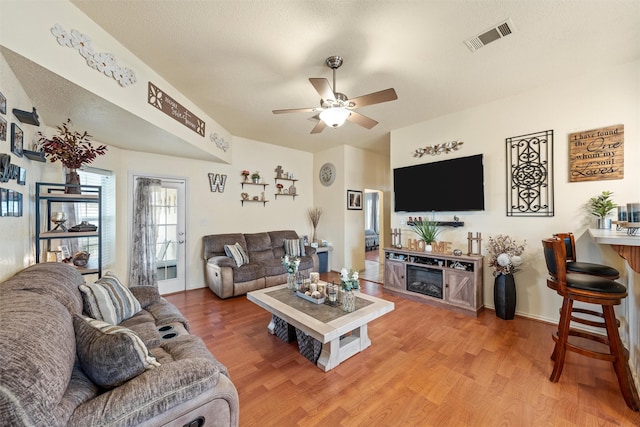 living area with light wood-style floors, visible vents, baseboards, and ceiling fan