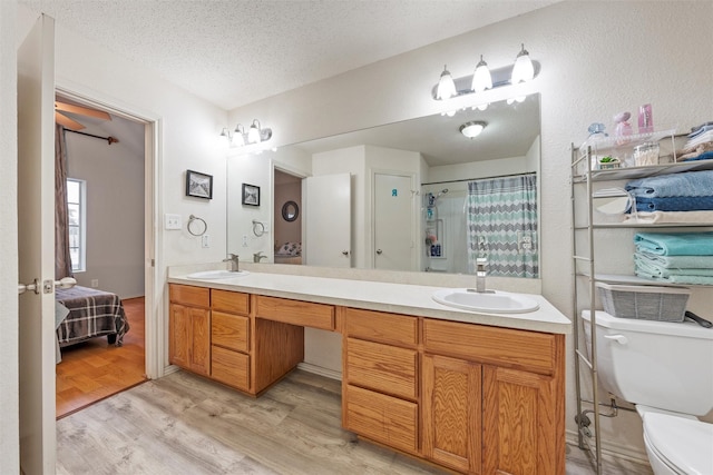 ensuite bathroom featuring double vanity, wood finished floors, toilet, and a sink