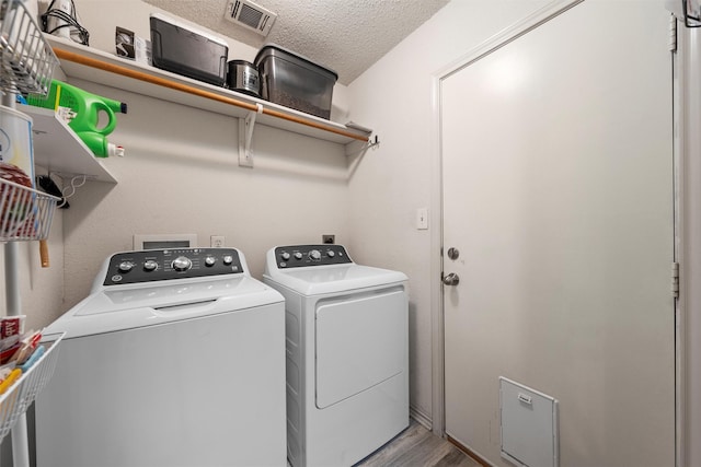 clothes washing area with washer and clothes dryer, laundry area, wood finished floors, visible vents, and a textured ceiling