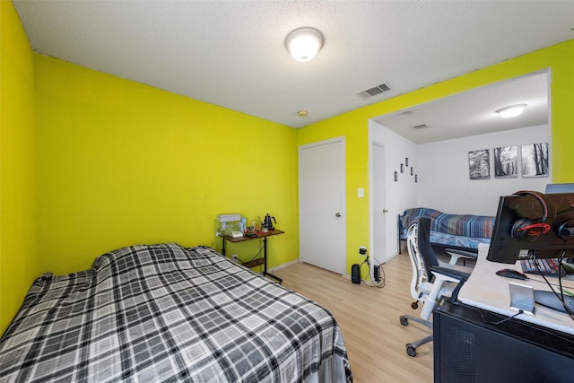 bedroom with a textured ceiling, visible vents, and light wood finished floors