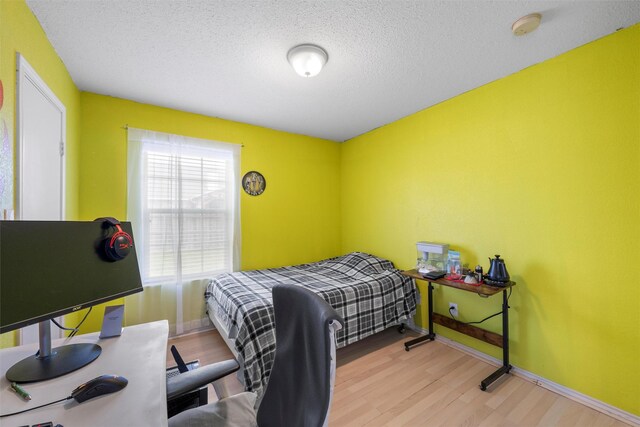 bedroom featuring baseboards, wood finished floors, and a textured ceiling