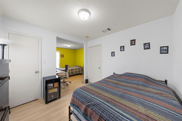 bedroom featuring light wood finished floors, visible vents, and a textured ceiling