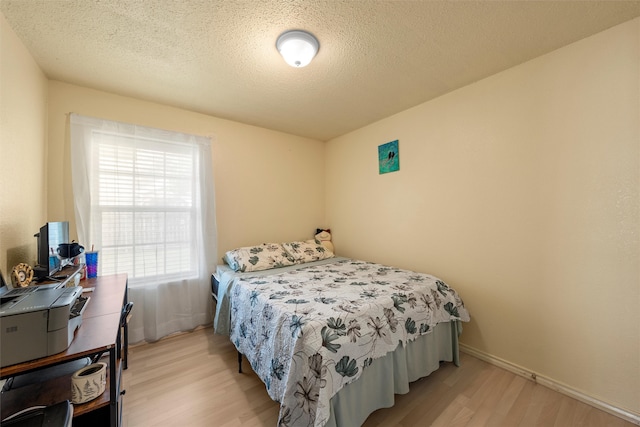 bedroom featuring light wood finished floors, baseboards, and a textured ceiling