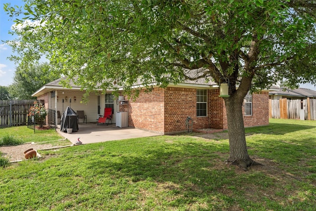 back of house featuring brick siding, a lawn, a patio, and fence