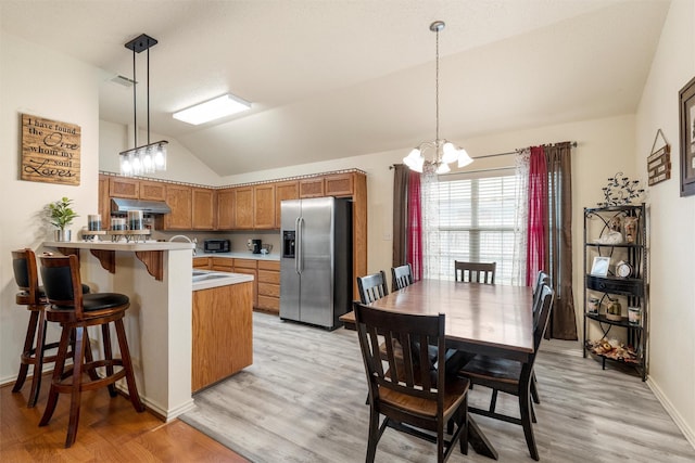 kitchen featuring lofted ceiling, under cabinet range hood, brown cabinets, stainless steel refrigerator with ice dispenser, and a notable chandelier