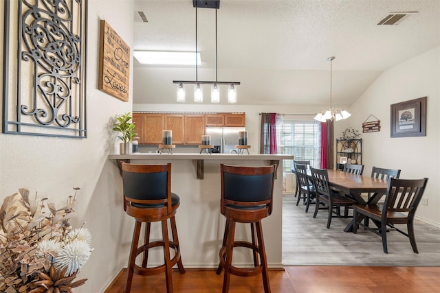 kitchen featuring visible vents, wood finished floors, brown cabinets, stainless steel fridge with ice dispenser, and a breakfast bar area