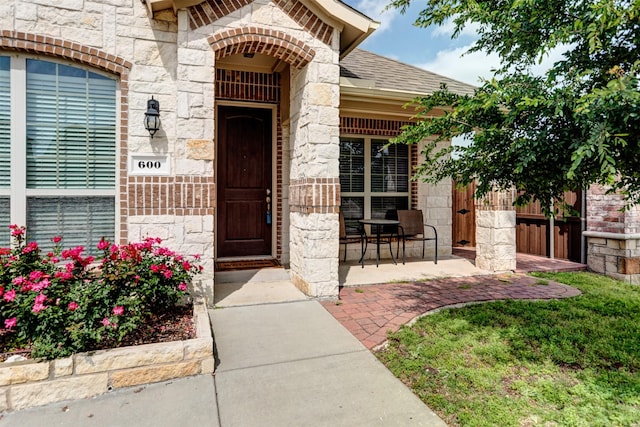 view of exterior entry with stone siding, a shingled roof, and fence