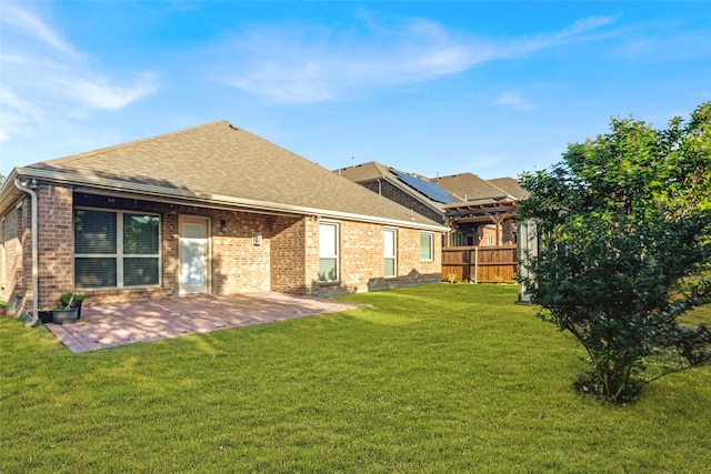 back of house with a yard, brick siding, fence, a patio, and roof with shingles