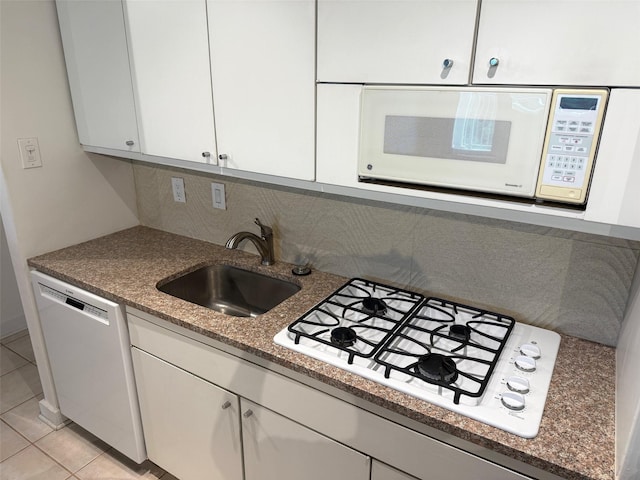 kitchen with a sink, decorative backsplash, white appliances, light tile patterned floors, and white cabinets