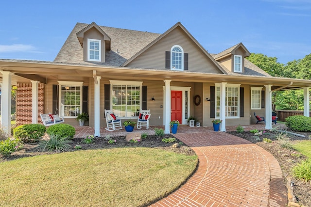 farmhouse-style home featuring a shingled roof, a front yard, and covered porch