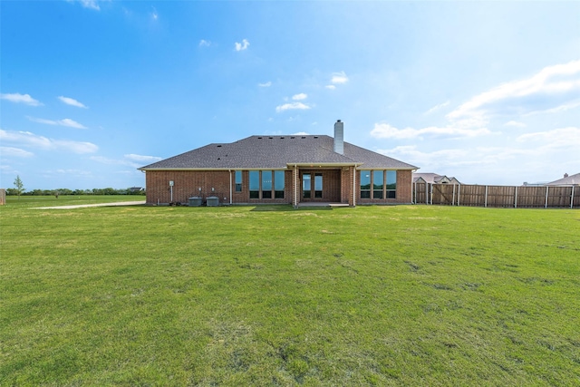 rear view of house featuring brick siding, a yard, a chimney, and fence