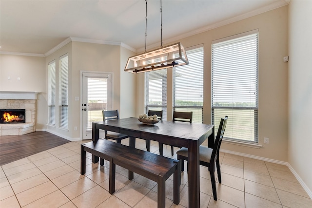dining space featuring light tile patterned flooring, a fireplace, crown molding, and baseboards