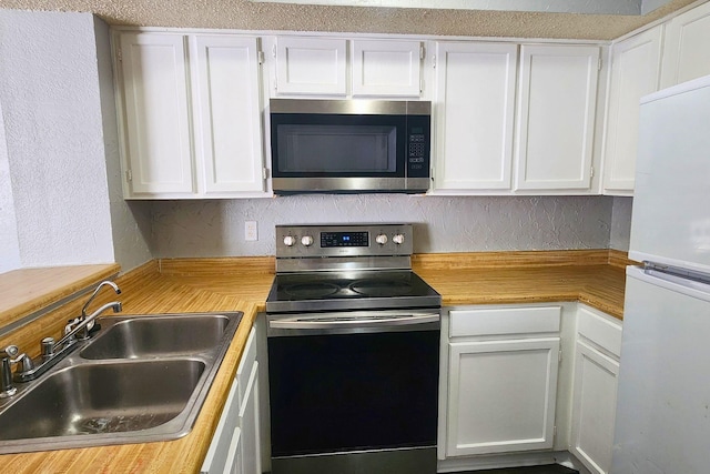kitchen with a textured wall, light countertops, white cabinets, a sink, and appliances with stainless steel finishes