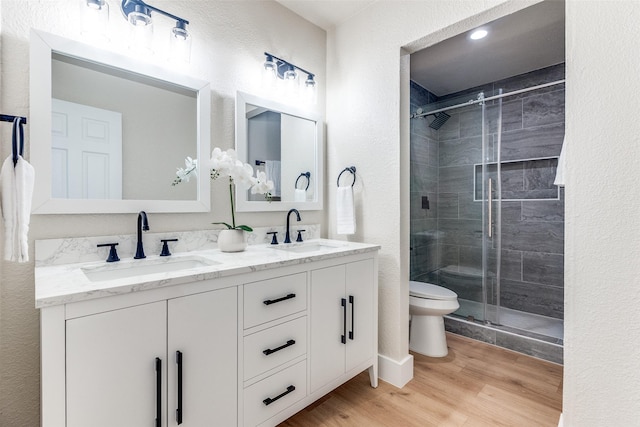 bathroom with a shower stall, toilet, wood finished floors, and a sink