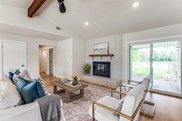 living area featuring a brick fireplace, visible vents, light wood finished floors, and lofted ceiling with beams