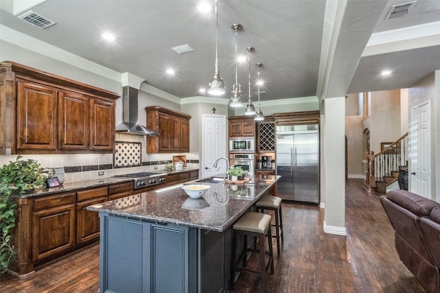 kitchen featuring built in appliances, wall chimney range hood, dark wood-style floors, and visible vents