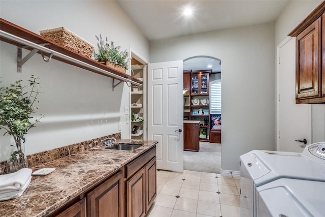 laundry room with a sink, arched walkways, washer and dryer, cabinet space, and light colored carpet