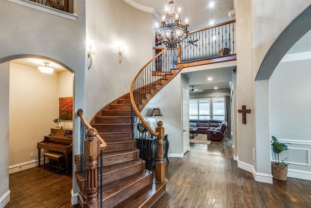 staircase with arched walkways, baseboards, a notable chandelier, a high ceiling, and wood finished floors