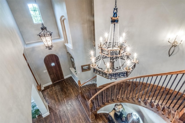 foyer with arched walkways, an inviting chandelier, wood finished floors, and stairs
