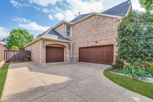view of front facade with driveway, fence, a garage, brick siding, and roof with shingles