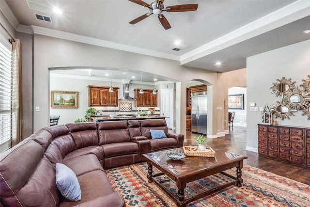 living area with wood finished floors, ceiling fan, arched walkways, ornamental molding, and visible vents