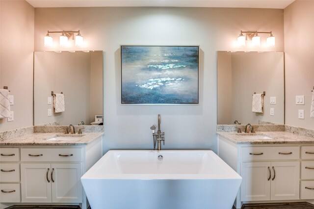 bathroom featuring two vanities, a soaking tub, and a sink