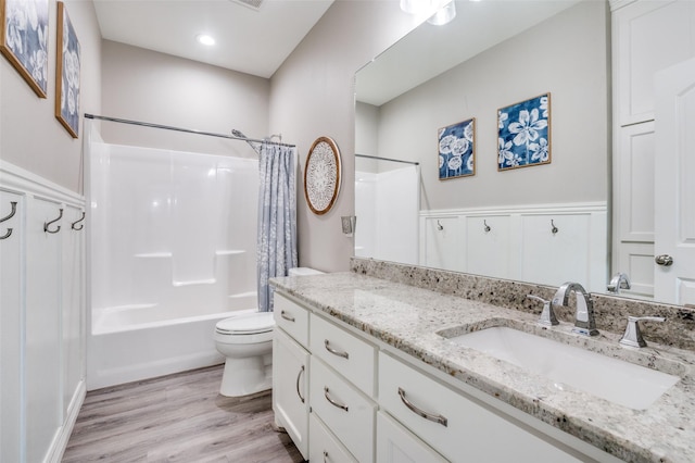 full bath featuring wood finished floors, wainscoting, vanity, shower / bathtub combination with curtain, and toilet