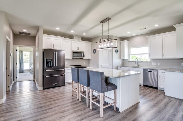 kitchen featuring white cabinets, stainless steel appliances, visible vents, a sink, and a center island