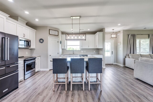 kitchen featuring light wood-type flooring, open floor plan, baseboards, a kitchen bar, and appliances with stainless steel finishes