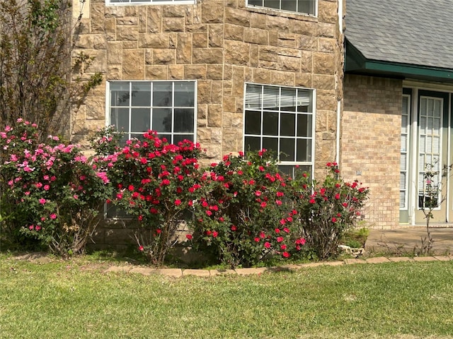 view of side of home featuring stone siding, roof with shingles, and a yard
