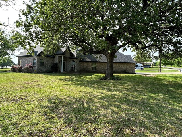 view of front facade with stone siding, a shingled roof, and a front lawn
