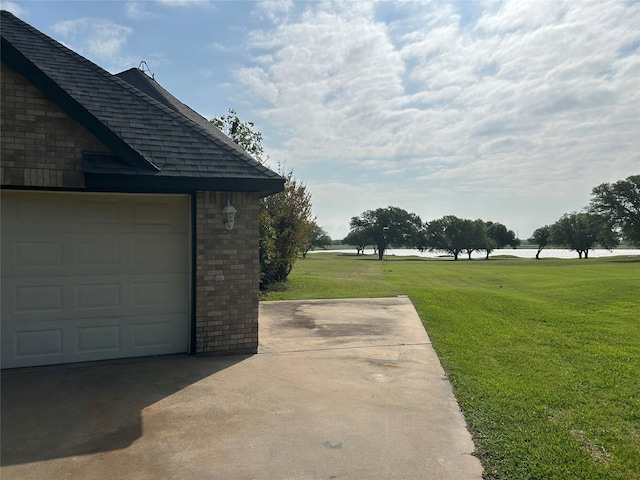 exterior space featuring brick siding, a yard, roof with shingles, and concrete driveway