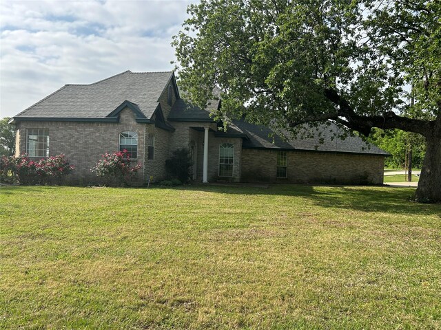 french country home with brick siding, a front lawn, and roof with shingles