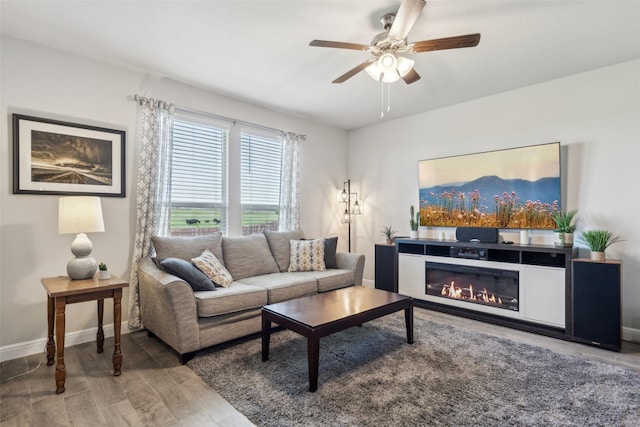 living room featuring ceiling fan, baseboards, a glass covered fireplace, and wood finished floors