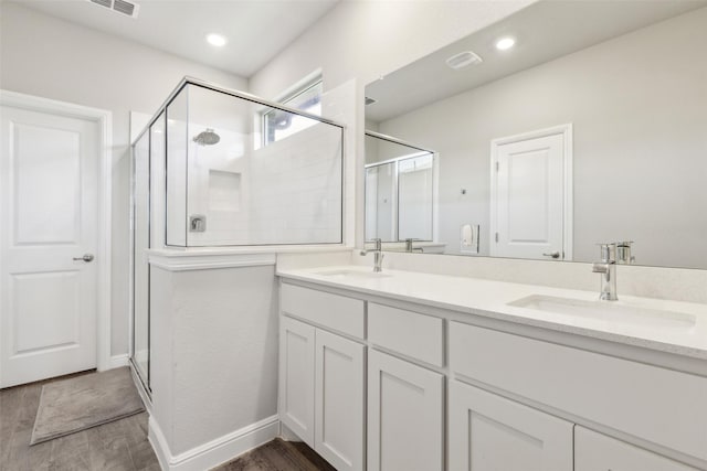 bathroom featuring double vanity, wood finished floors, a stall shower, and a sink