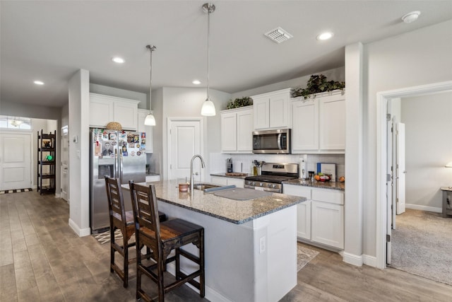 kitchen featuring stainless steel appliances, dark stone countertops, visible vents, a sink, and a kitchen island with sink