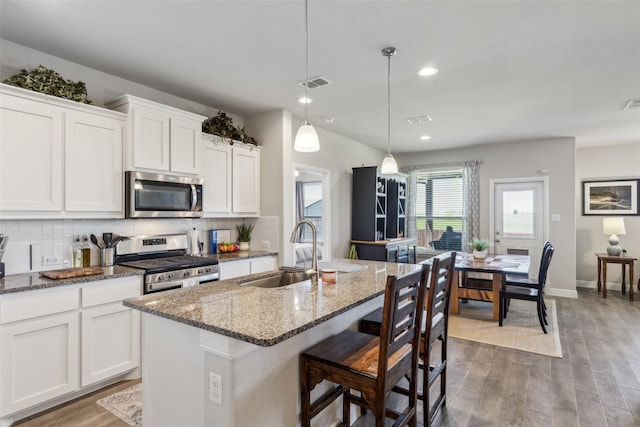 kitchen featuring a sink, a kitchen island with sink, white cabinets, appliances with stainless steel finishes, and visible vents