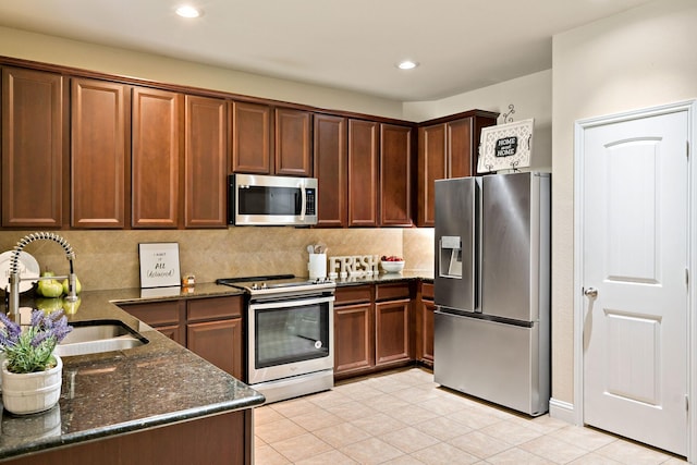 kitchen with decorative backsplash, appliances with stainless steel finishes, dark stone countertops, and a sink