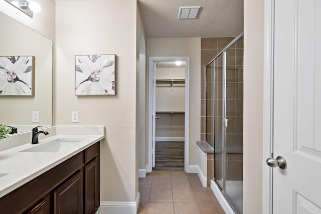 full bath featuring tile patterned floors, a sink, a stall shower, visible vents, and a spacious closet