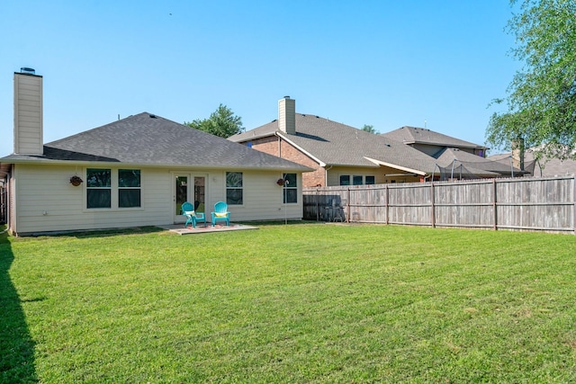 rear view of house featuring roof with shingles, a fenced backyard, a chimney, a patio area, and a yard