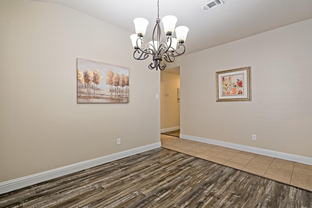 empty room featuring wood finished floors, visible vents, baseboards, and an inviting chandelier