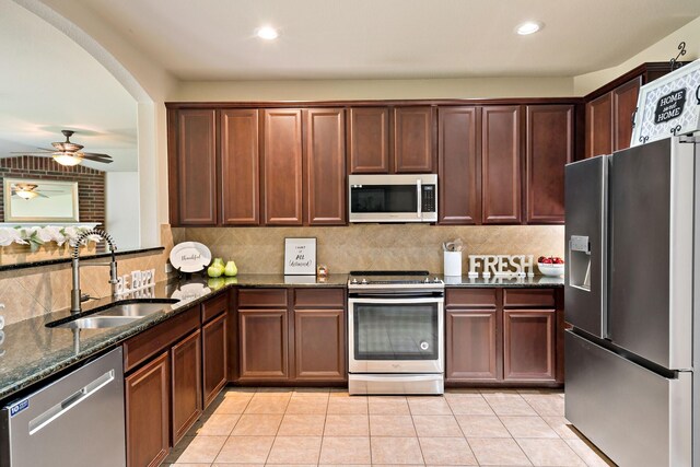 kitchen featuring dark stone counters, a sink, decorative backsplash, light tile patterned floors, and appliances with stainless steel finishes