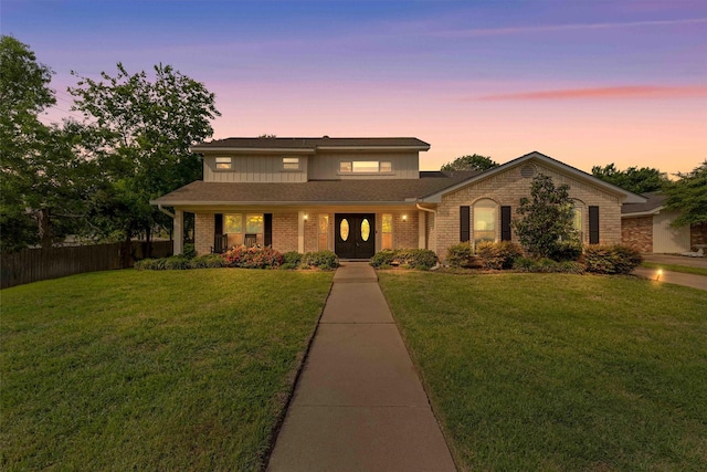 traditional-style house with fence, brick siding, a front yard, and roof with shingles