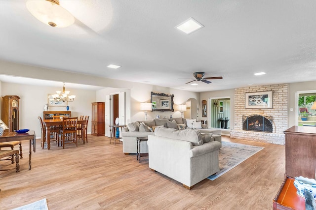 living area featuring arched walkways, light wood-style floors, a brick fireplace, and ceiling fan with notable chandelier