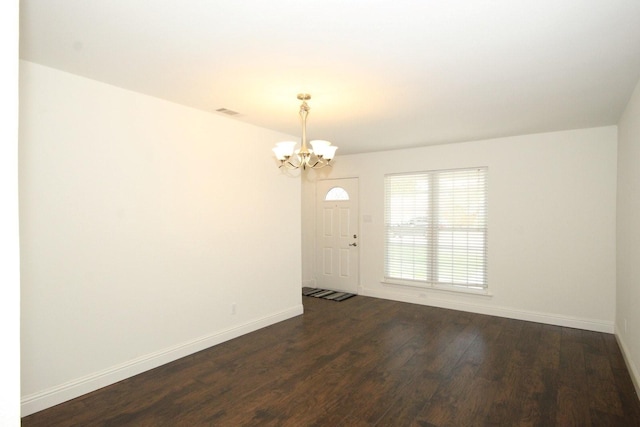 unfurnished room with baseboards, a notable chandelier, dark wood-type flooring, and visible vents