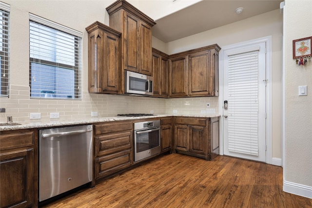7305 Caladium Dr, Mckinney, TX 75070 - kitchen featuring appliances with stainless steel finishes, backsplash, dark wood-style flooring, light stone counters, and baseboards